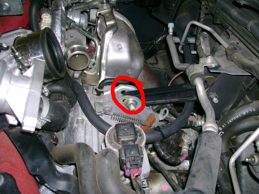 Subaru STi: Unbolt the lower pitch stop bolt. Now that the IC is out of the way, access is easy and it is circled in red. Use a 14mm wrench on the nut with a 14mm socket and breaker bar on the bolt head. Once loose, remove the bolt and tilt the pitch stopper up as far as it can go.